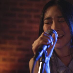 Woman singing into microphone with eyes closed